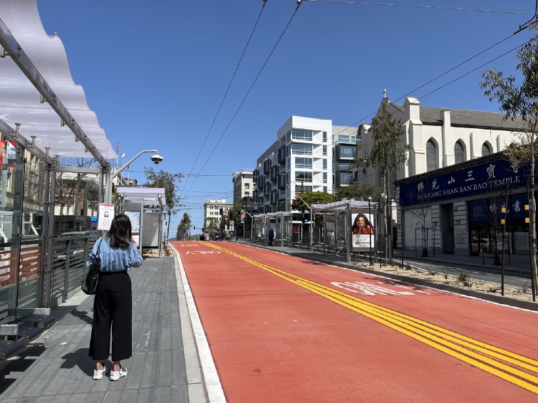 A view of the dedicated red bus lanes on San Francisco’s Van Ness Avenue. A rider waits on one of the platforms. There’s no bus in view.