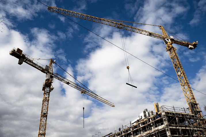 Two construction cranes framed against sky with clouds