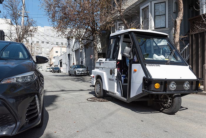 A three-wheeled parking enforcement vehicle with license plate readers attached to its roof drives down a quiet road.